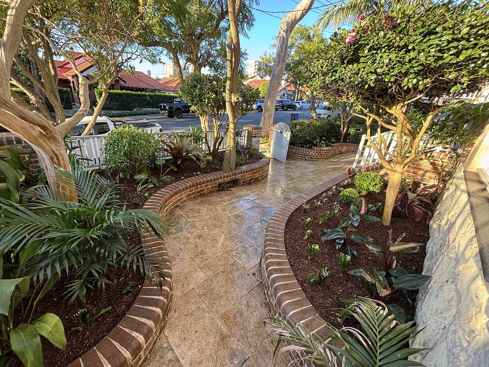 Curving paved path between brick-edged tropical garden beds